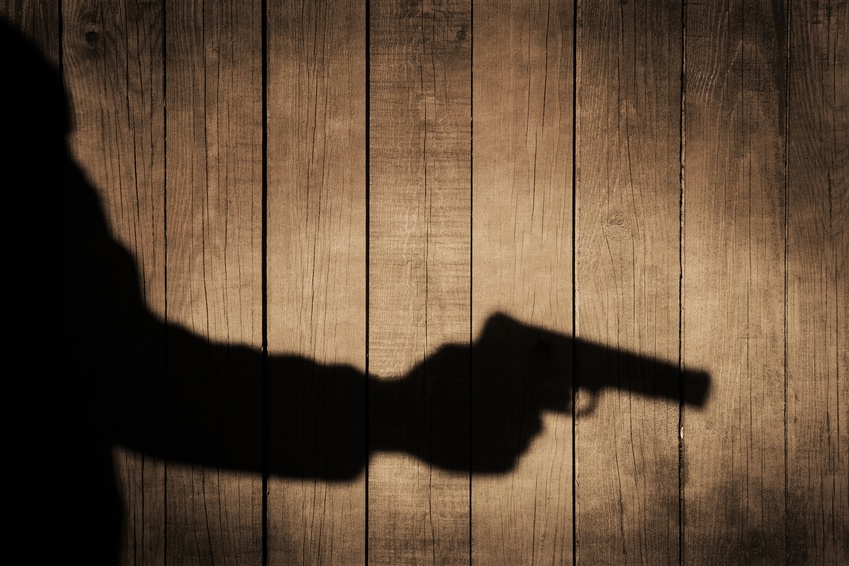 Outstretched arm with a gun. Black shadow on natural wooden background, with space for text or image.